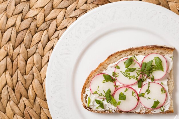 Wholegrain sandwich with organic radish and cream cheese on white plate and straw table mat