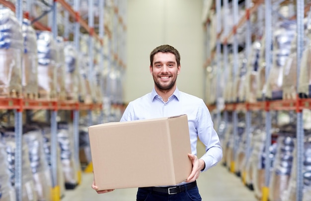 wholesale, logistic, business, export and people concept - happy man with cardboard parcel box at warehouse