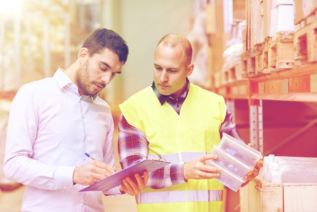 Foto concetto di vendita all'ingrosso, logistica, persone ed esportazione - operai manuali e uomini d'affari con clipboard e scatole nel magazzino