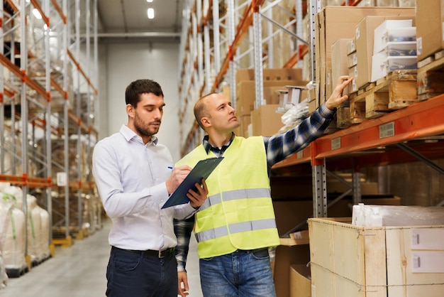 wholesale, logistic, people and export concept - manual worker and businessmen with clipboards at warehouse