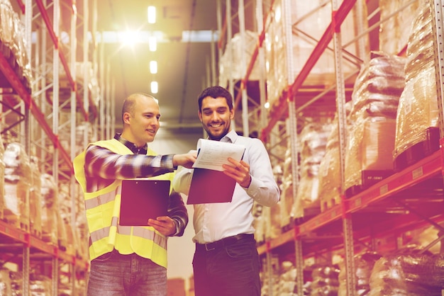 wholesale, logistic, people and export concept - manual worker and businessmen with clipboards at warehouse