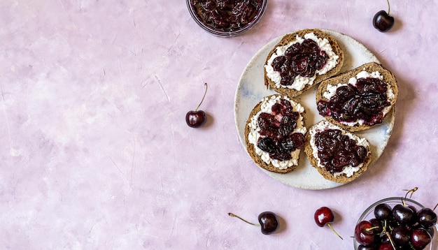 Toast integrali con ricotta e marmellata di ciliegie dolci fatta in casa sulla piastra vista dall'alto copia spazio