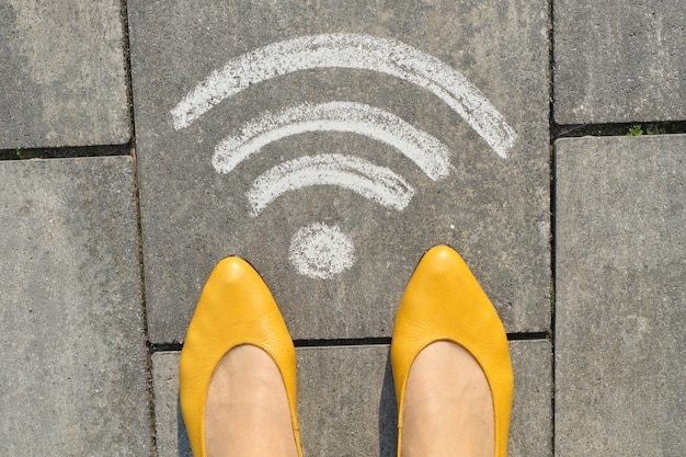 Foto wi-fi symbool op grijze stoep met benen van de vrouw, bovenaanzicht