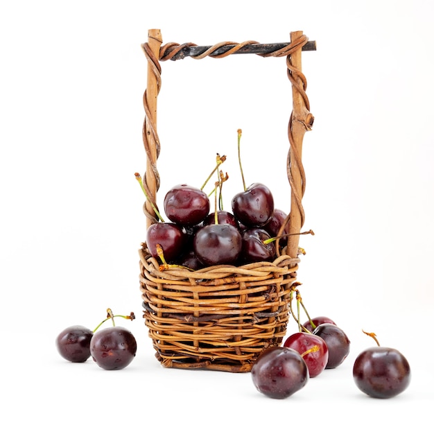 Wicker basket full of ripe sweet cherries on white background