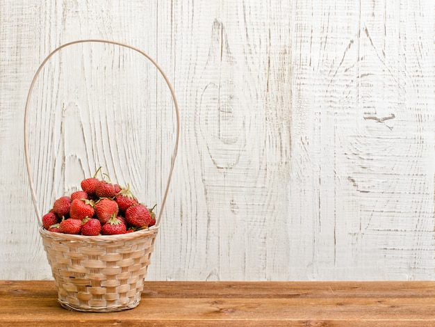 Photo wicker basket of ripe strawberries standing on a brown table on white wooden background