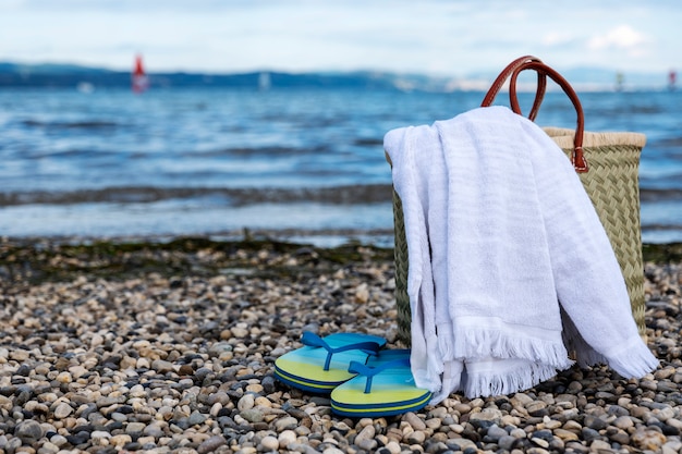 Фото Плетеная корзина, полотенце и тапочки на каменистом пляже на фоне красивого неба