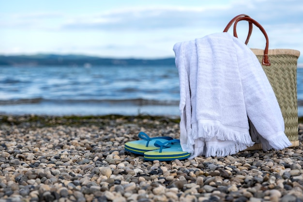 Wicker basket, towel and slippers on a rocky beach against a beautiful sky