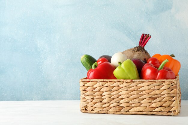 Wicker basket and vegetables on white wooden 