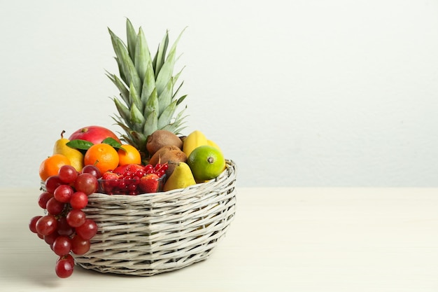 Wicker basket with different fresh fruits on white wooden table Space for text