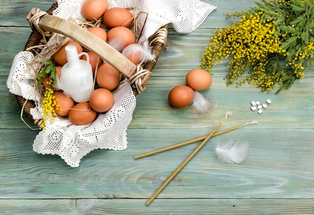 Wicker basket with eggs branches of mimosa holy water candles and incense on a wooden background closeup