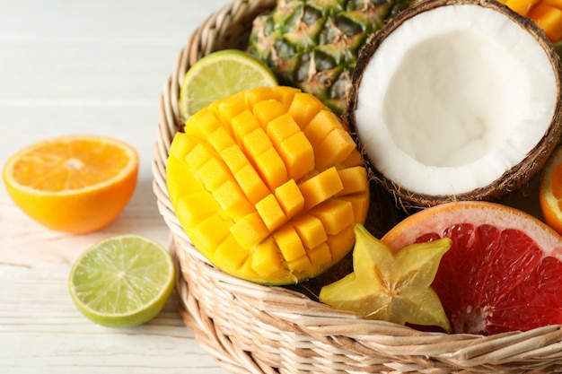 Wicker basket with exotic fruits on white wooden background, close up