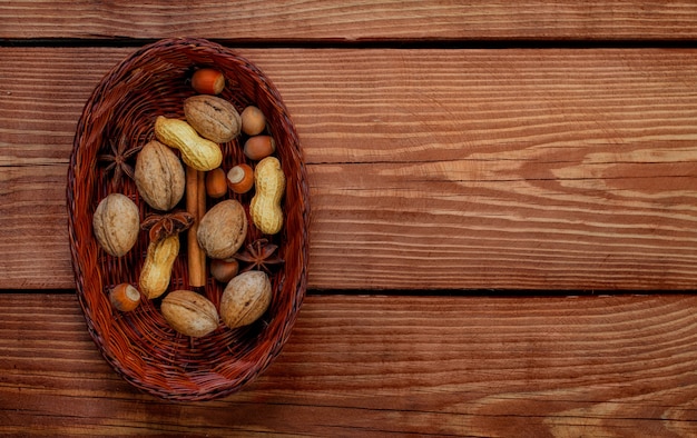 Wicker basket with hazelnut, walnut, peanut and spices  on textured wooden background. Top of view.