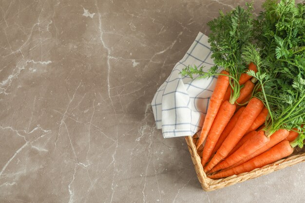 Wicker basket with ripe carrots on grey table, space for text