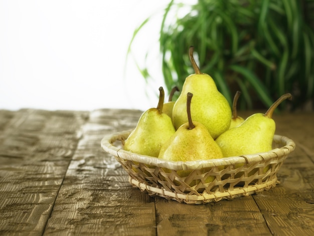 Wicker basket with ripe pears on a wooden table.