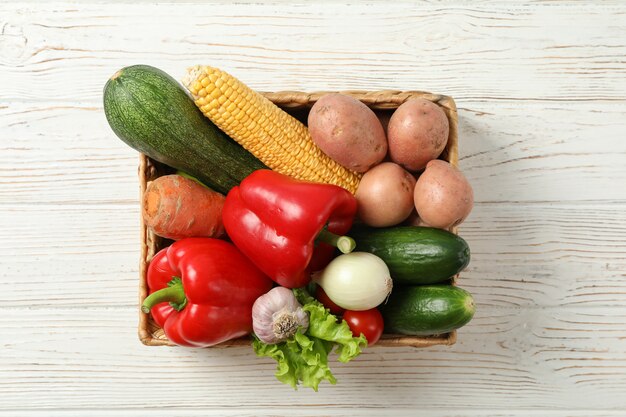 Wicker basket with vegetables on white wooden 