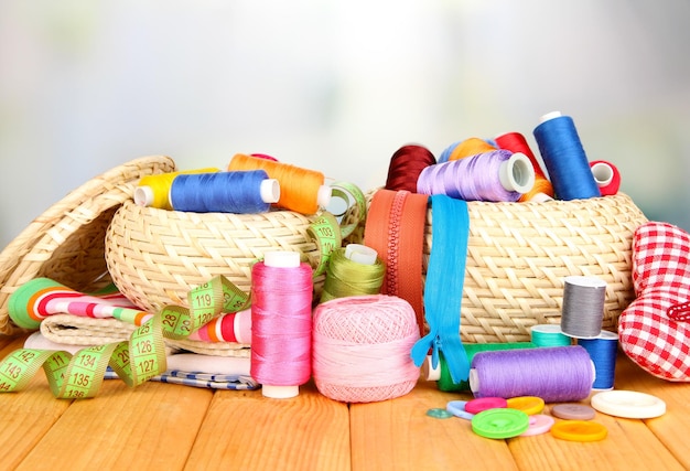 Wicker baskets with accessories for needlework on wooden table on bright background