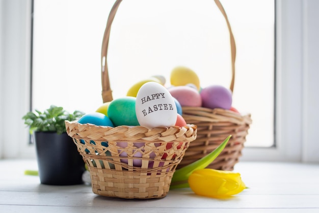 Photo wicker baskets with bright colorful eggs and with text happy easter and flower