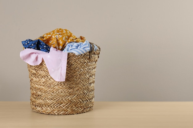 Photo wicker laundry basket with different clothes on wooden table space for text