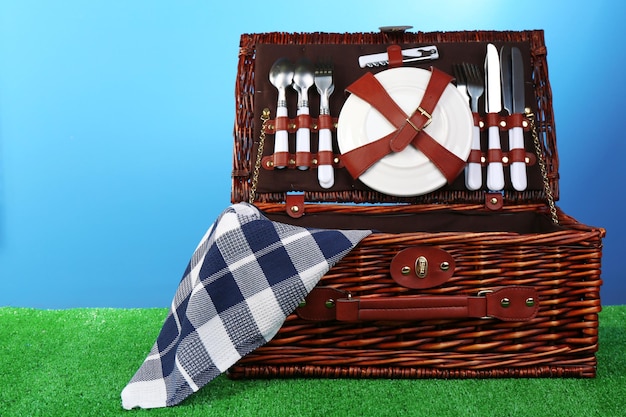 Wicker picnic basket on green grass on blue background