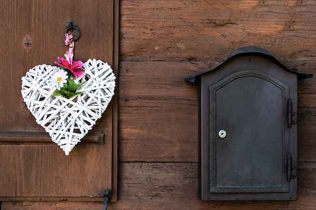 Photo a wicker white heart with peonies and daisies hangs on a wooden shutter and a mailbox next to it.