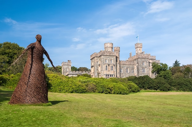 Wicker woman statue and castle in stornoway, united kingdom. willow sculpture on green grounds of lews castle estate. architecture and design. landmark and attraction. summer vacation and wanderlust