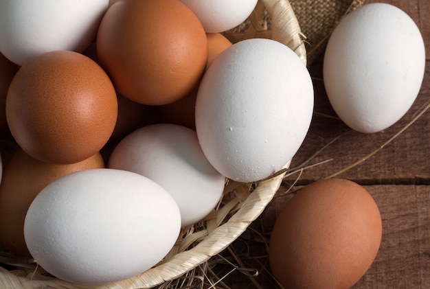 Wicker wooden plate with brown and white eggs on a wooden background, top view.