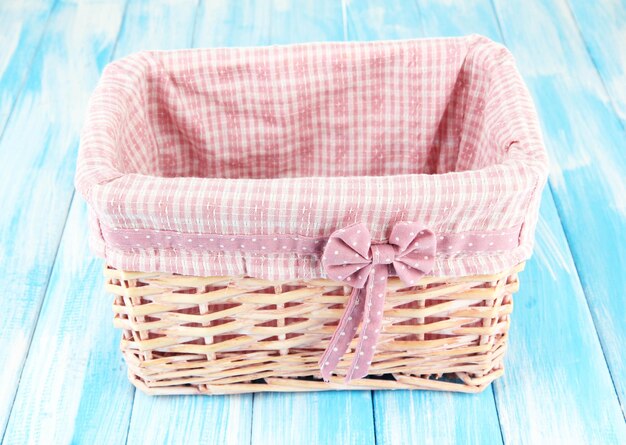 Photo wicket basket with pink fabric and bow on color wooden background