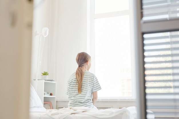 Wide angle Back view at lonely child in hospital room, shot from doorway, copy space