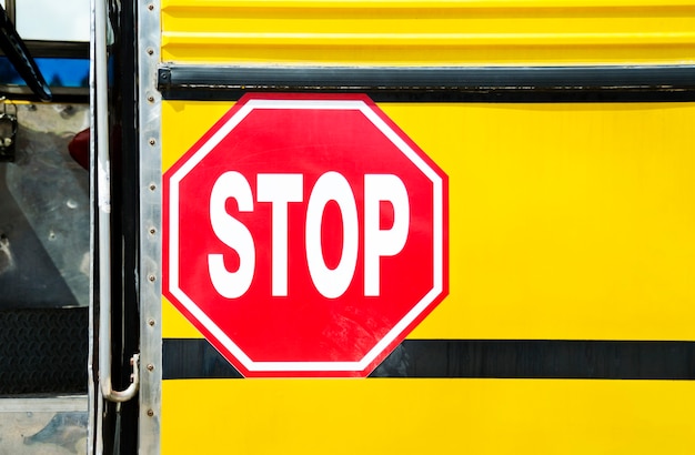 Foto vista frontale grandangolare di uno scuolabus giallo arancio brillante e del grande segnale di stop rosso