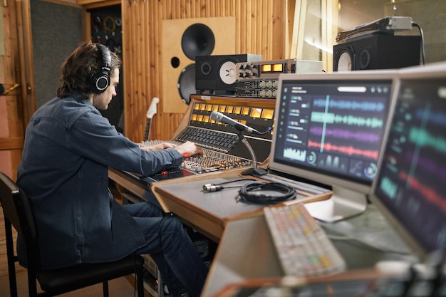 Wide angle at music producer operating audio workstation in professional recording studio copy space