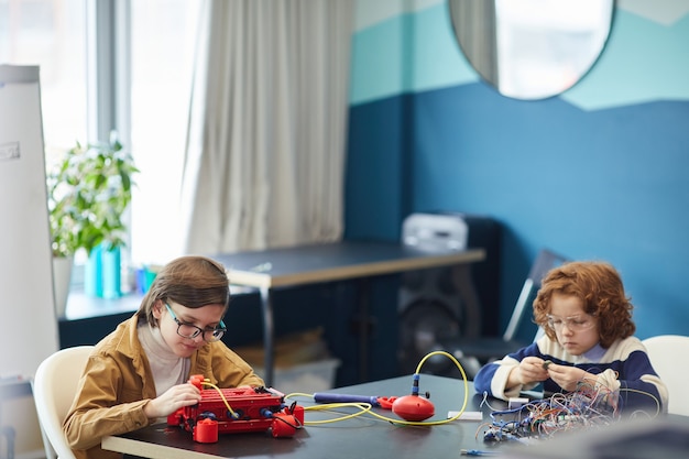 Ritratto grandangolare di due ragazzi che costruiscono robot mentre si godono la lezione di ingegneria nella scuola di sviluppo, copia spazio