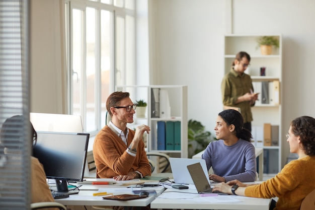 Wide angle portrait of young business team discussing startup project while working at desk in white office interior, copy space