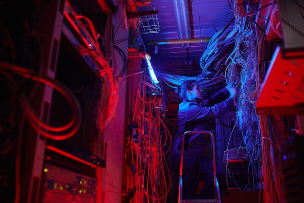 Wide angle portrait of young man setting up computer network in server room with cables and wires, copy space