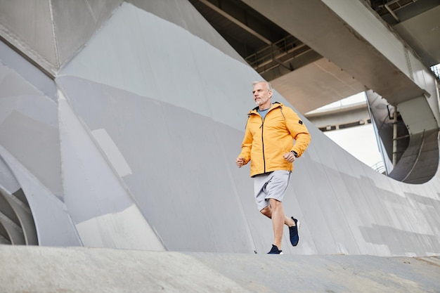 Wide angle shot of senior man running outdoors in urban city setttting against concrete background