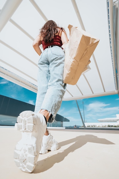 Wide angle shot of a woman holding shopping bags entering the\
mall, sunny day and fancy clothes, modern styling and young woman\
concepts