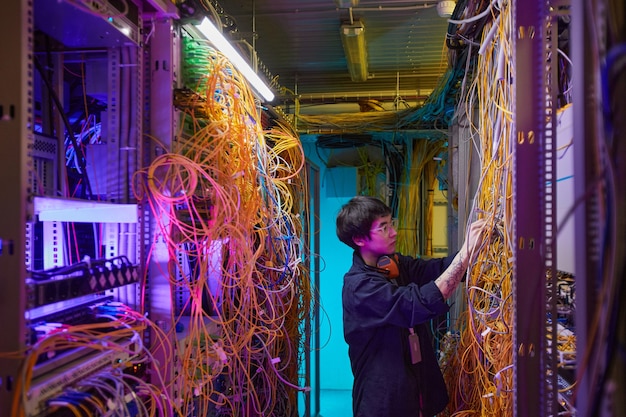 Wide angle side view at young network technician connecting wires and cables in server room, copy space