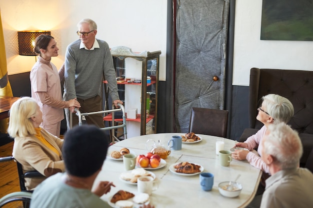 Wide angle view at diverse group of senior people enjoying\
breakfast at dining table in nursing home...