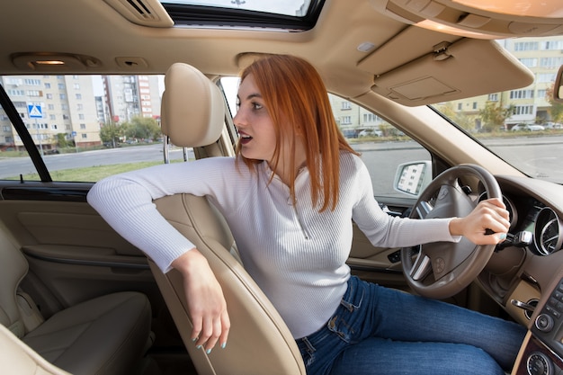 Фото Широкоугольный вид молодой рыжий женщина водитель за рулем автомобиля, оглядываясь назад.