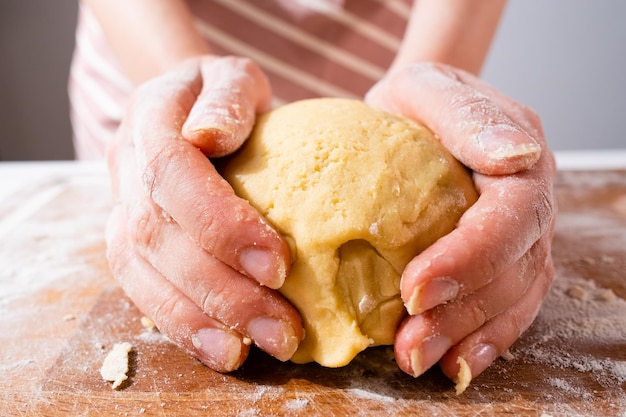 Ampio angolo della mano della donna che impasta l'impasto per i bidoni della pizza o i pan di zenzero sulla scrivania di legno