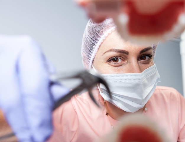 Photo wide angle woman professional dentist about to pull out tooth with forceps at dental clinic