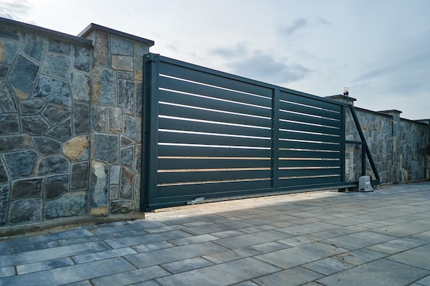 Wide automatic sliding gate with remote control installed in high stone fense wall Security and protection concept