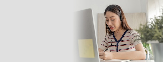 Wide banner. asian girl student studying online with headset
and laptop computer at home, network communication, online meeting,
video call conference, internet technology and online education
concept