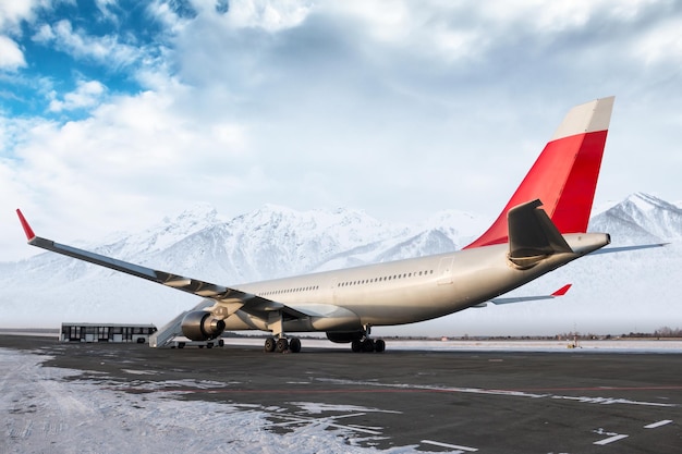 Wide body passenger airliner with staircase at airport apron on background of high scenic mountains