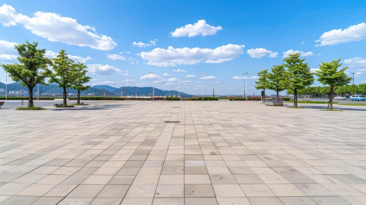 Photo 포장 된 표면과 가장자리를 은 나무가 있는 넓은  빈 도시 광장 하늘은 밝은 파란색으로 색 구름이 있습니다.