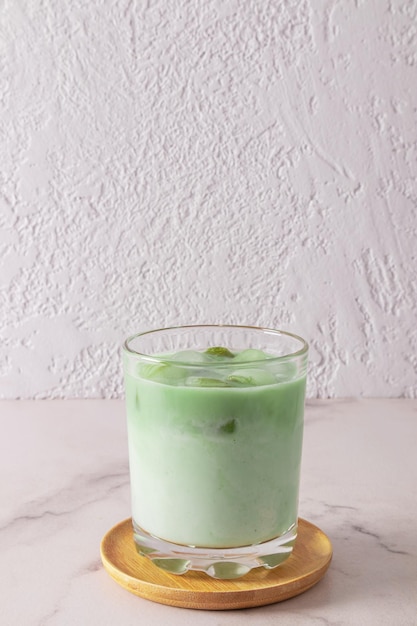 A wide glass of natural green tea matcha latte stands on a wooden plate and a marble white table healthimproving invigorating agent