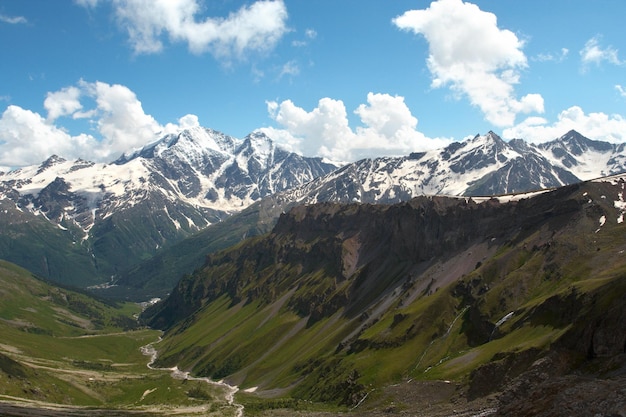 Wide green valley and mountains river with snowed peaks in the distance