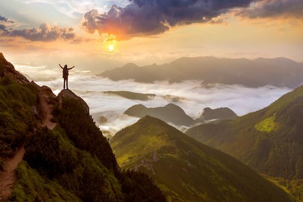 宽山全景照片。小轮廓与背包旅游在岩石山坡上举起的手在山谷覆盖着白色的白云。美丽的大自然,旅游和旅行的概念