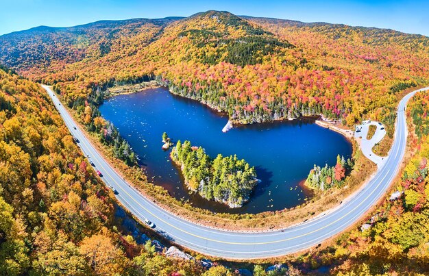 Wide panorama aerial over highway through stunning peak fall foliage New Hampshire mountains around