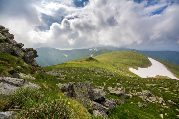 Ampio panorama illuminato dal plateau della montagna del sole con erba verde, macchie di neve e grandi massi sulle montagne lontane sotto la scena del cielo nuvoloso. bellezza della natura, turismo e concetto di viaggio.