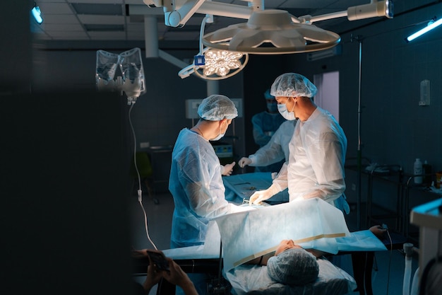 Wide shot of cooperating team of surgeons processing surgical operation in dark operating room